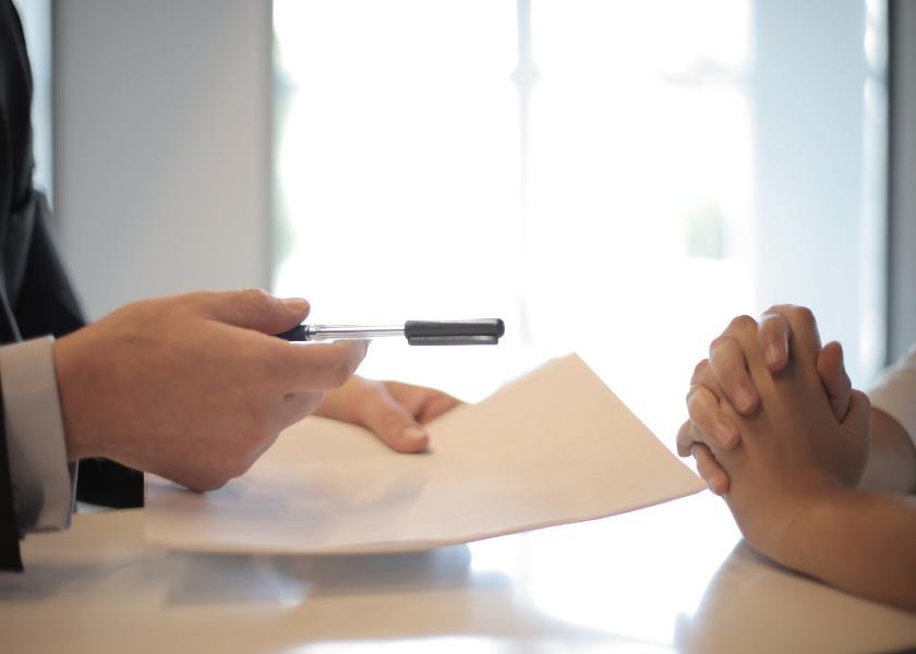 A person giving a pen and paper to another set of hands across the table.