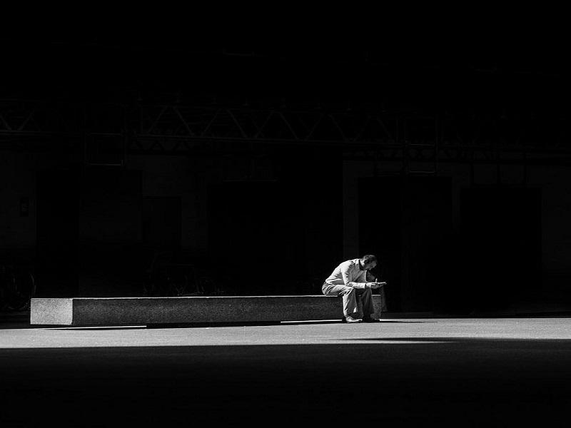 Man sat on a bench alone in a solitary moment with a dark background