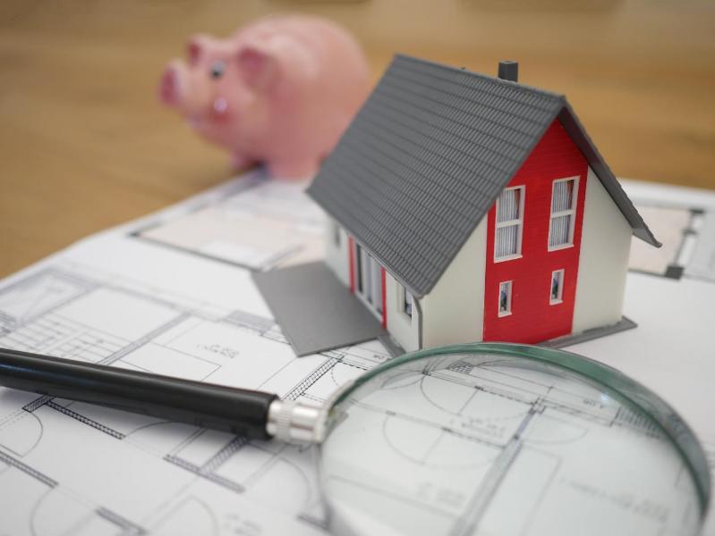 A model house and magnifying glass with a piggy bank in the background