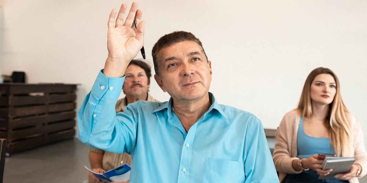 A man with his hand up in a classroom.