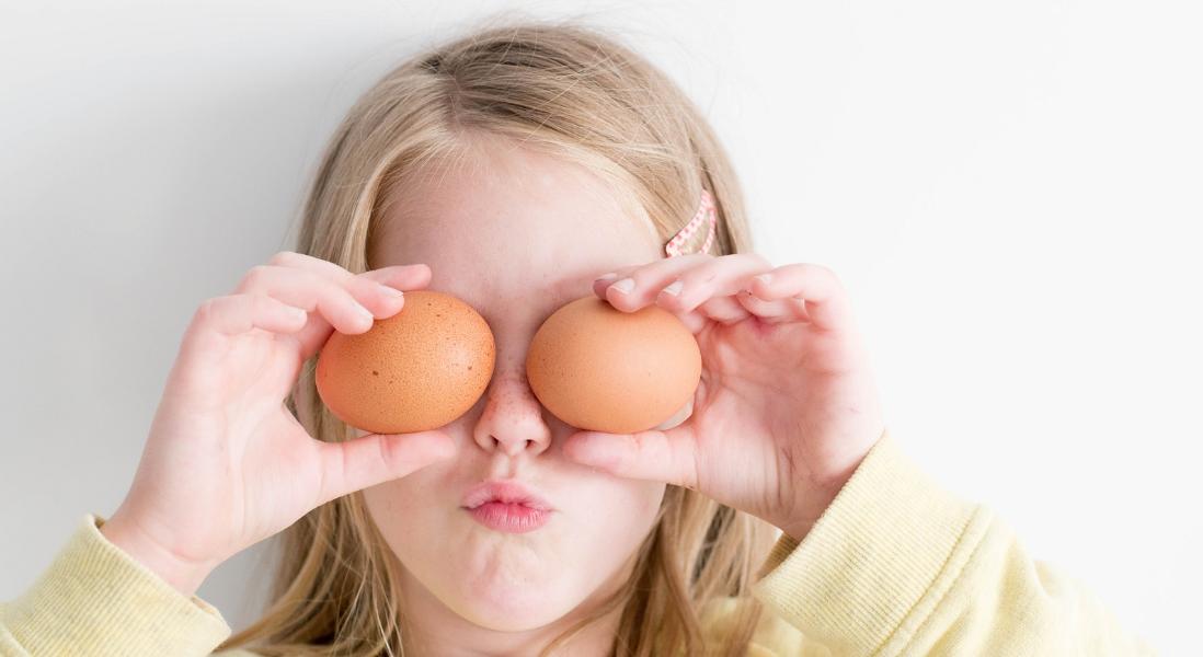 A little girl with blonde hair using two eggs as eyes.