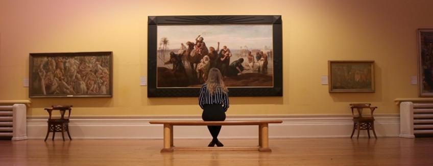 A lady sat on a bench at the Harris Museum looking at paintings