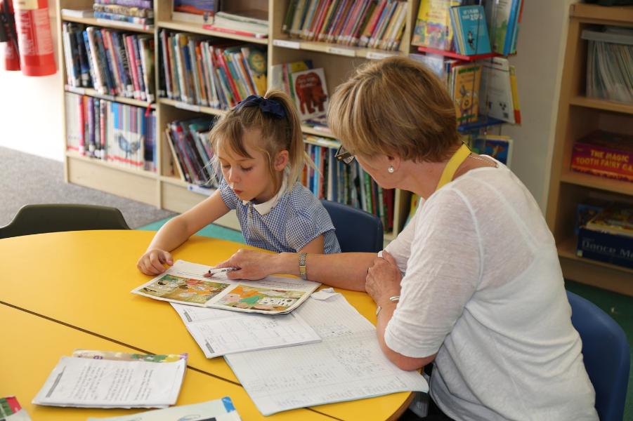 A lady sat reading with a little girl in a school library.