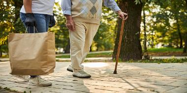 Senior man with crutch and female helping with purchase