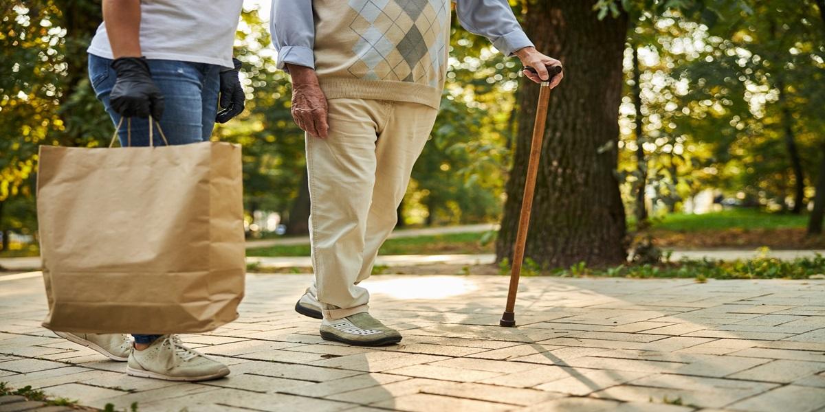 Senior man with crutch and female helping with purchase