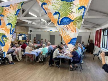 A community hall with people sat chatting with bunting with Flamingos on them.