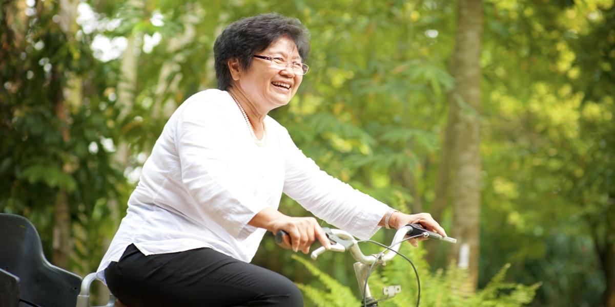 60s senior Asian woman riding on bicycle outdoor with great fun