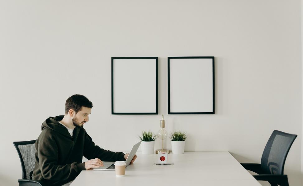 Man in a hoodie sat at a table looking at his lap top