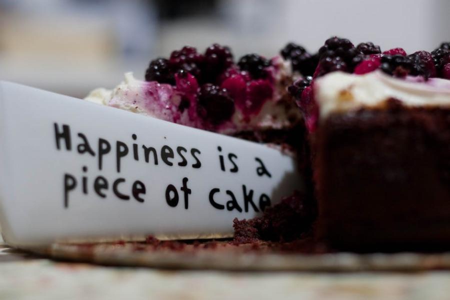 A slice of cake with a piece of paper saying happiness is a piece of cake