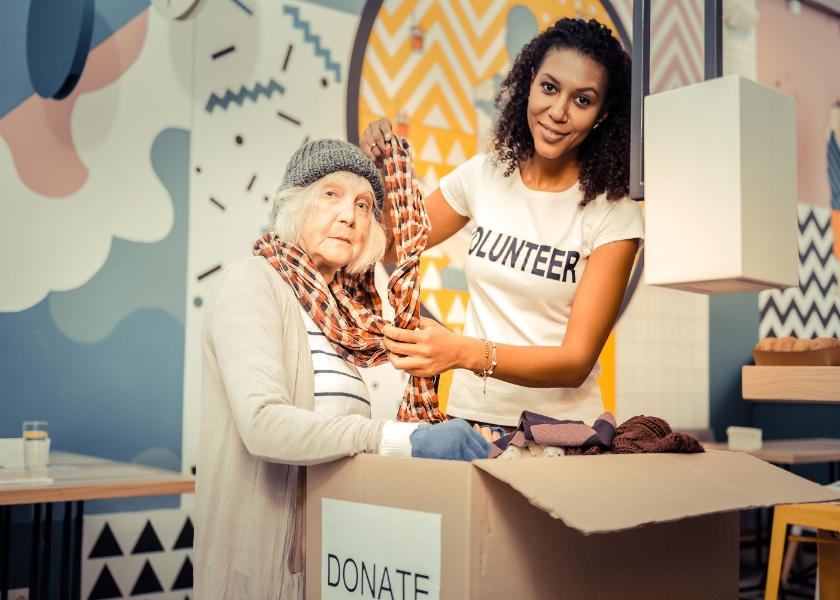 Try it on. Pleasant afro American woman smiling while helping a homeless woman to wear a scarf