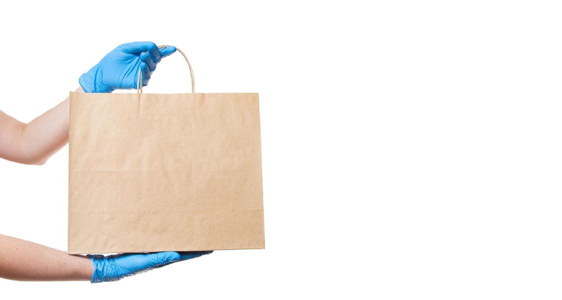 Hands in sterile gloves of a courier for the safe delivery of food in eco-friendly craft label package during quarantine of coronavirus covid-19 pandemic isolated on white background with copy space.