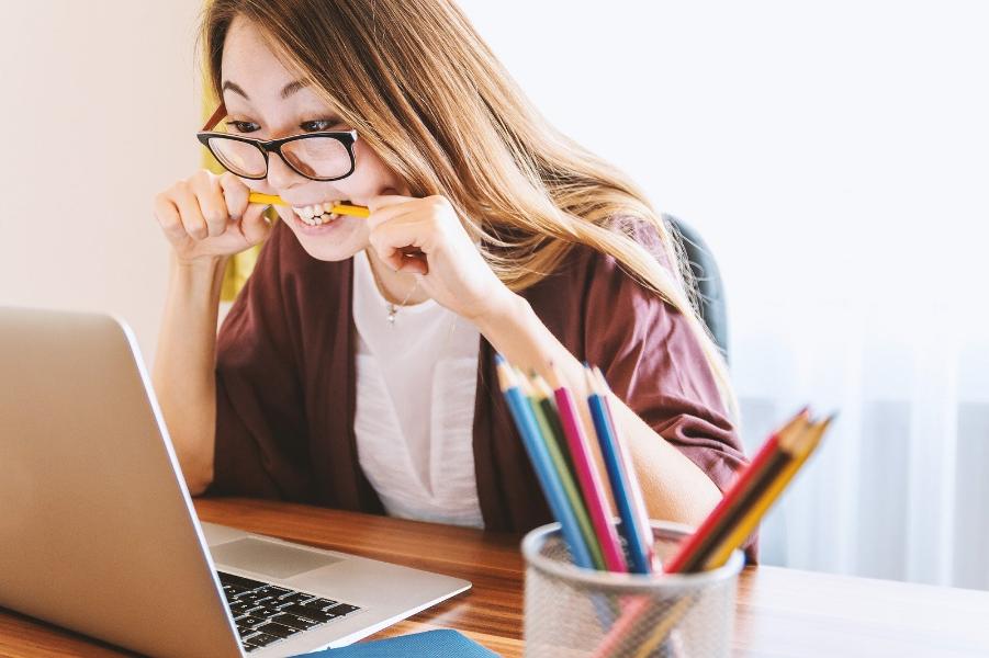 Lady sat looking at her laptop with a pencil in her mouth