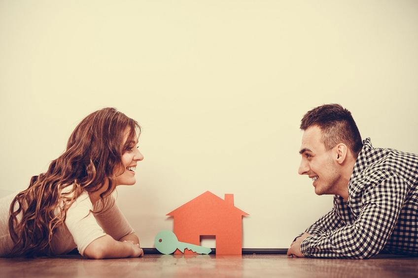 A lady and a man laid on the floor putting a paper key into a paper house