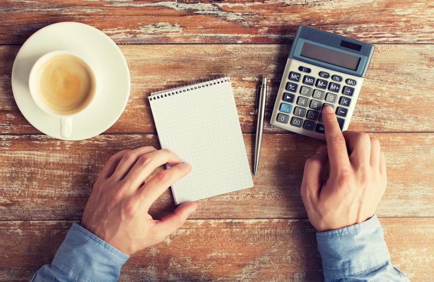 A person with a notepad, coffee and a calculator on a table