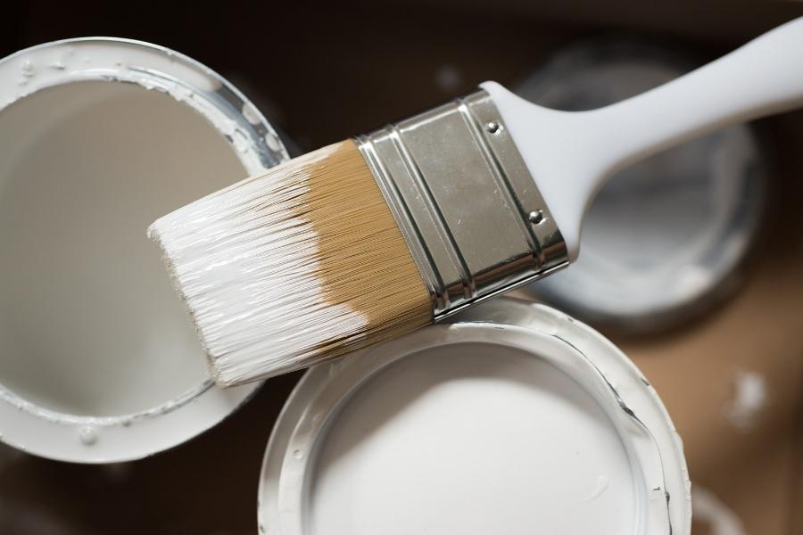 Two pots of white paint with a brush on the top