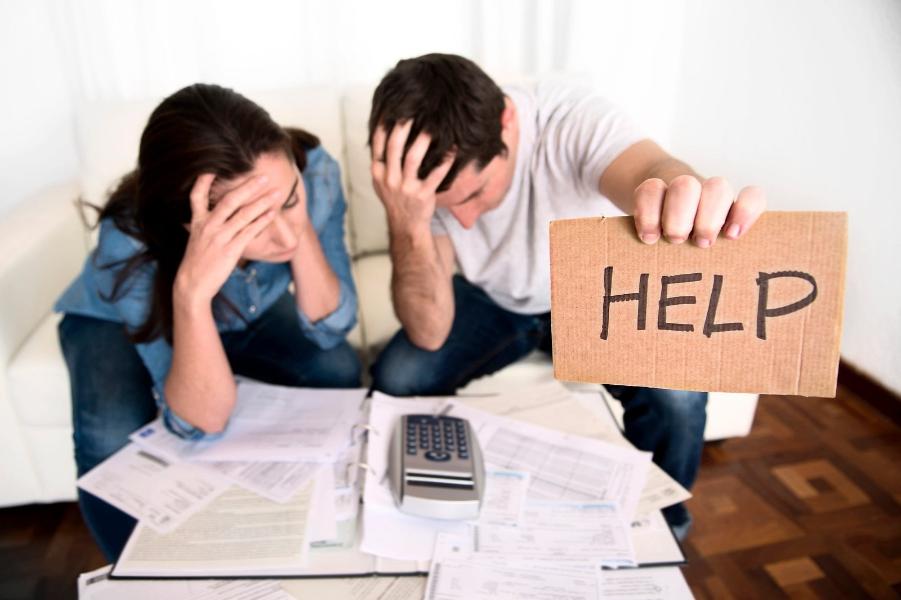 A couple looking overwhelmed with a help sign written on cardboard 